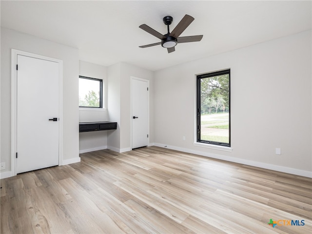 unfurnished bedroom featuring multiple windows, light wood-style flooring, baseboards, and a ceiling fan
