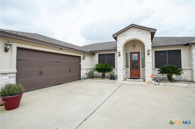 view of front of home with an attached garage, roof with shingles, stucco siding, stone siding, and driveway