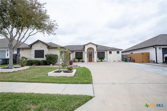 view of front of house with concrete driveway, fence, stone siding, and a front yard