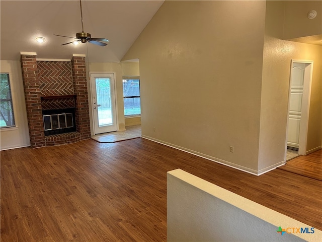 unfurnished living room with a brick fireplace, ceiling fan, wood-type flooring, and high vaulted ceiling