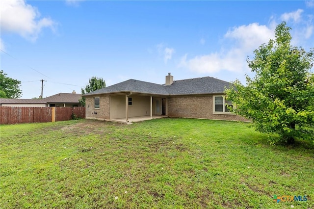 rear view of house with a yard, a chimney, brick siding, fence, and a patio