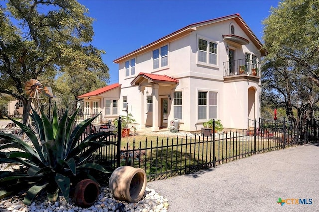 view of front facade with stucco siding, a balcony, a fenced front yard, and a front lawn