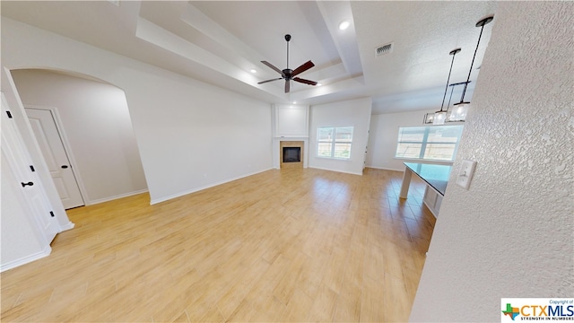 unfurnished living room with light hardwood / wood-style floors, ceiling fan, and a tray ceiling