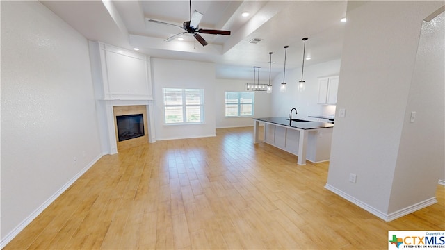 unfurnished living room with a tray ceiling, light hardwood / wood-style flooring, ceiling fan, and sink