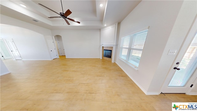 unfurnished living room with ceiling fan, a towering ceiling, and a tray ceiling