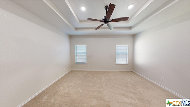 unfurnished room featuring ceiling fan, a raised ceiling, and light carpet