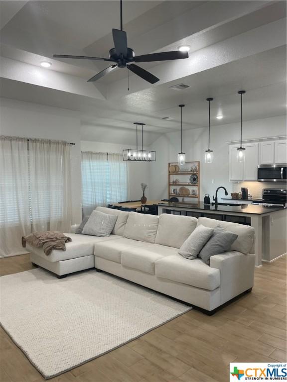 living room with sink, light hardwood / wood-style floors, and ceiling fan with notable chandelier