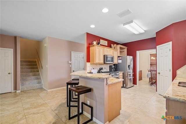 kitchen with a kitchen breakfast bar, visible vents, appliances with stainless steel finishes, light stone counters, and light brown cabinets