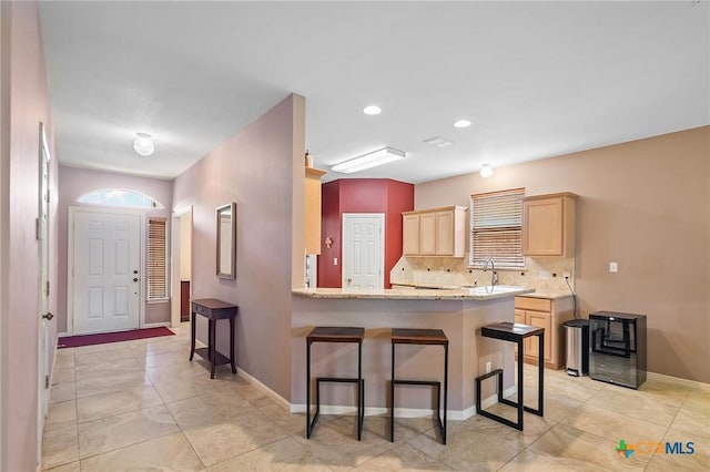 kitchen featuring decorative backsplash, a peninsula, light brown cabinetry, and a kitchen bar