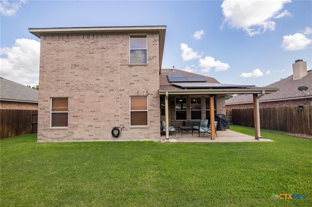 back of property featuring solar panels, brick siding, a fenced backyard, a yard, and a patio