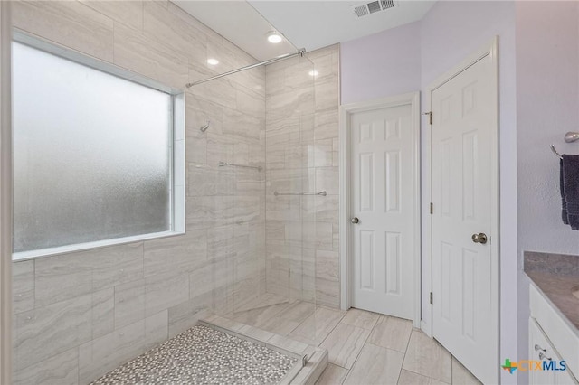 bathroom with vanity, a tile shower, and visible vents