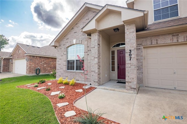 doorway to property featuring an attached garage, a yard, driveway, and brick siding