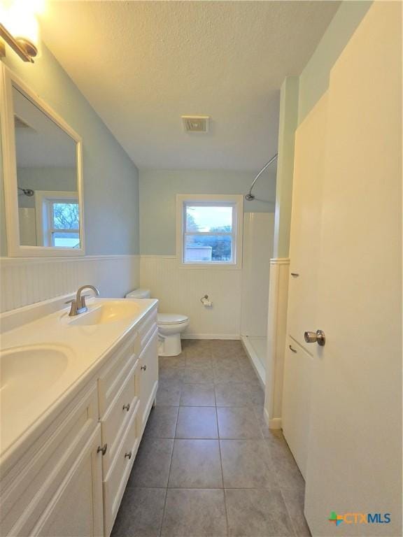 bathroom with walk in shower, toilet, a textured ceiling, vanity, and tile patterned flooring