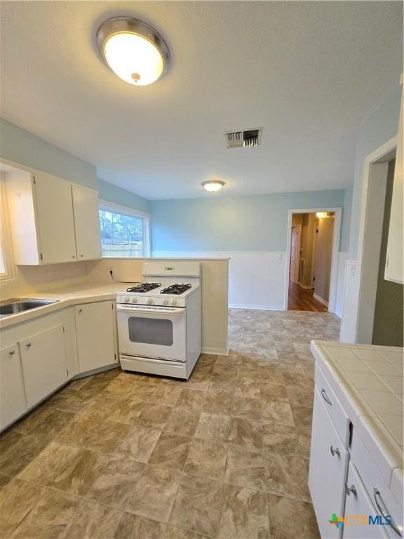 kitchen with tile countertops, sink, white range with gas stovetop, and white cabinets