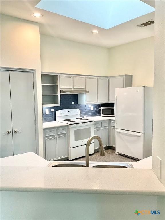 9100 Brimstone Ln, Austin, TX 78717 - kitchen featuring white appliances, a skylight, gray cabinets, decorative backsplash, and recessed lighting