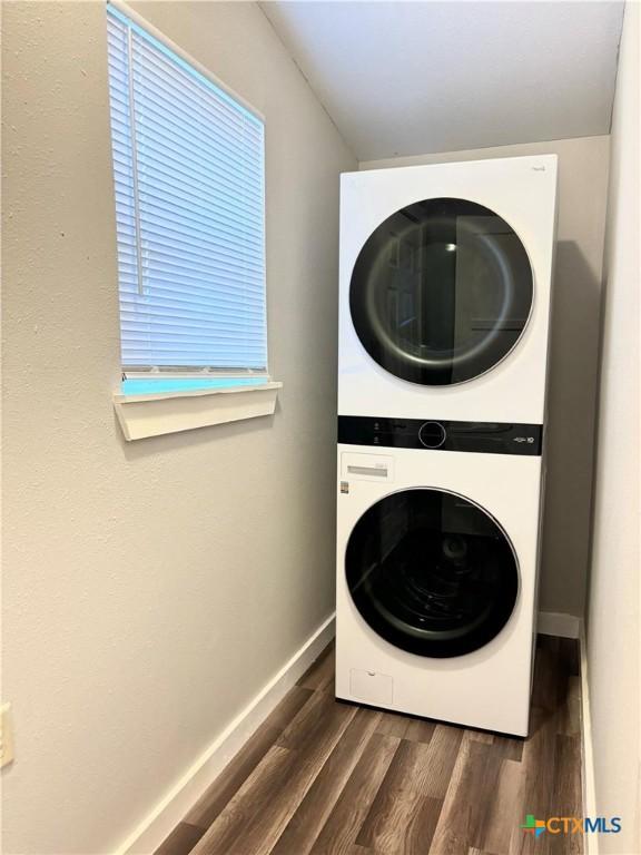 laundry room featuring stacked washer / drying machine and dark hardwood / wood-style flooring