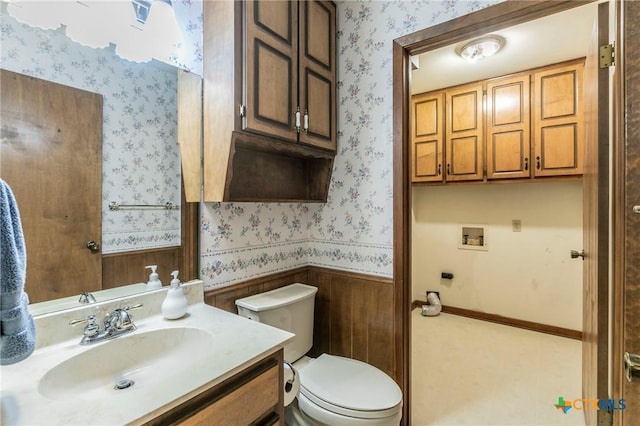 half bath with wainscoting, vanity, toilet, and wallpapered walls