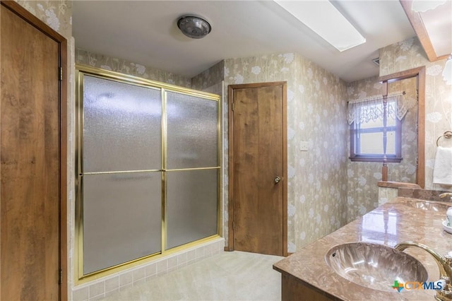 bathroom featuring a stall shower, double vanity, a sink, and wallpapered walls