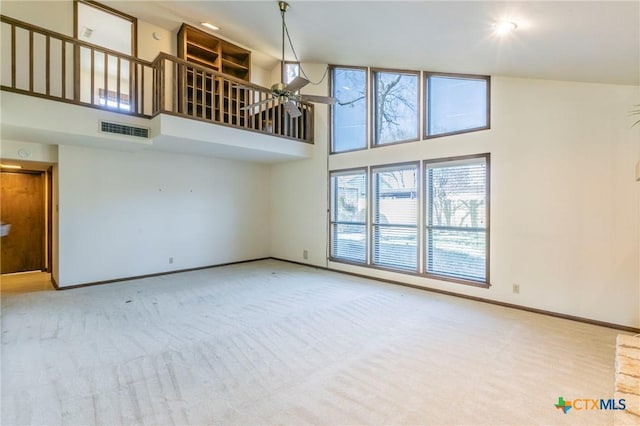 unfurnished living room with carpet, visible vents, a towering ceiling, ceiling fan, and baseboards