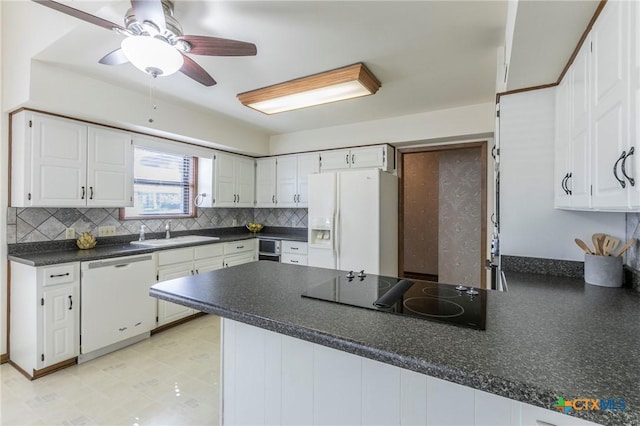 kitchen featuring dark countertops, white cabinets, a sink, white appliances, and a peninsula