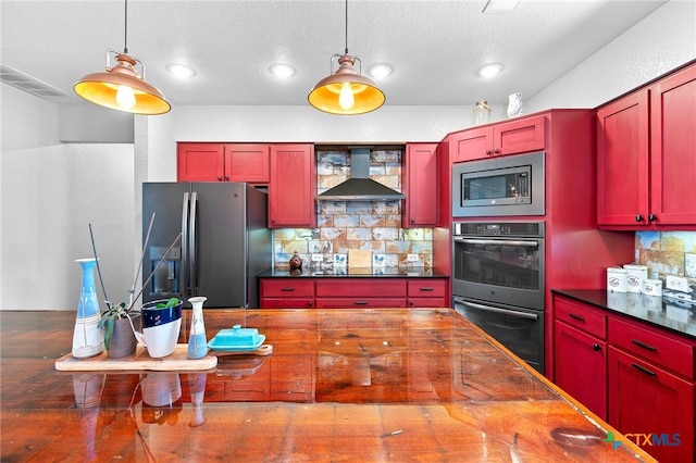 kitchen with hanging light fixtures, wall chimney range hood, backsplash, and appliances with stainless steel finishes