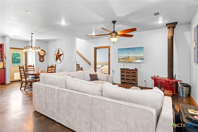 living room with ceiling fan with notable chandelier, a wood stove, and a textured ceiling