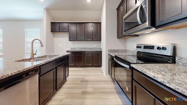 kitchen featuring sink, light stone countertops, light wood-type flooring, appliances with stainless steel finishes, and dark brown cabinets