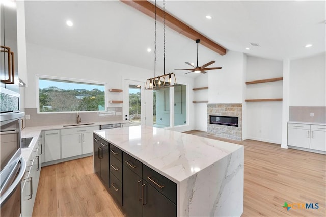 kitchen with pendant lighting, sink, white cabinetry, a center island, and light stone counters