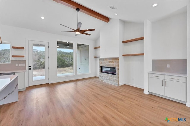 unfurnished living room featuring a stone fireplace, plenty of natural light, lofted ceiling with beams, and light hardwood / wood-style floors