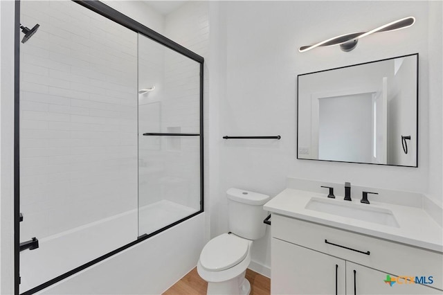 full bathroom featuring hardwood / wood-style flooring, vanity, shower / bath combination with glass door, and toilet