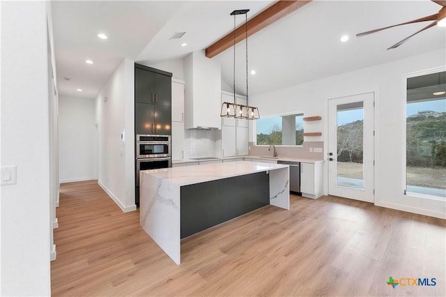 kitchen featuring appliances with stainless steel finishes, hanging light fixtures, a center island, light stone counters, and light wood-type flooring