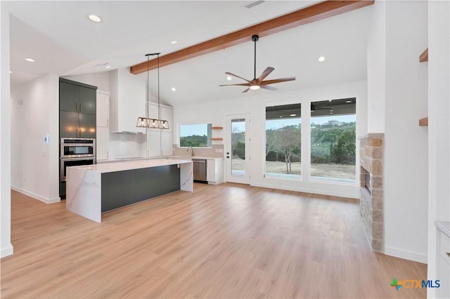 kitchen with appliances with stainless steel finishes, a kitchen island, decorative light fixtures, light hardwood / wood-style floors, and beam ceiling