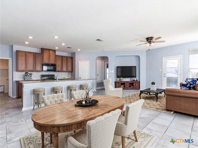 kitchen featuring black appliances, ceiling fan, a center island with sink, and backsplash