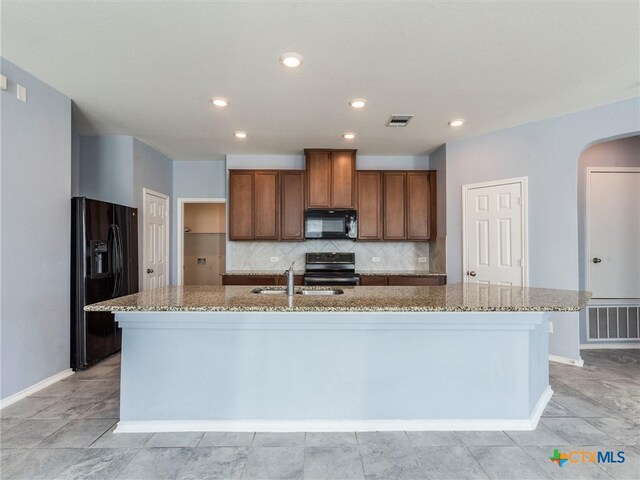 kitchen featuring black appliances, light stone counters, sink, and an island with sink