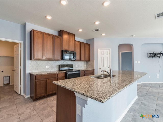 kitchen with black appliances, light stone counters, sink, and a kitchen island with sink