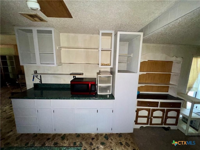 235 Murray Ln, Gatesville, TX 76528 - kitchen with dark countertops, a textured ceiling, and white cabinetry