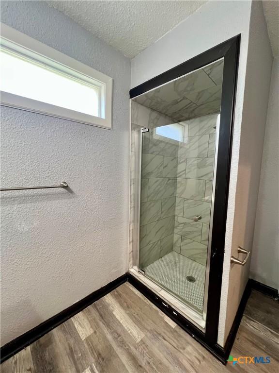 bathroom with wood-type flooring, an enclosed shower, and a textured ceiling