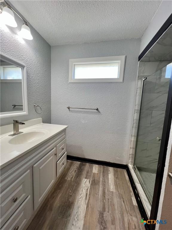 bathroom featuring vanity, wood-type flooring, a shower with door, and a textured ceiling