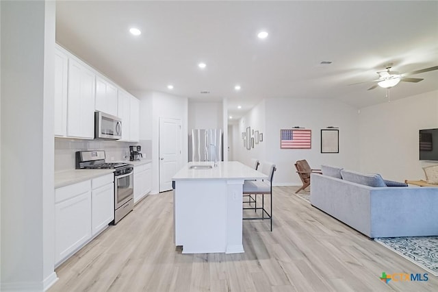 kitchen with stainless steel appliances, a kitchen bar, white cabinets, and an island with sink