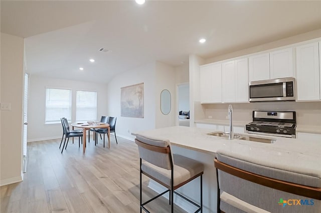 kitchen with light wood-type flooring, stainless steel appliances, white cabinets, and a breakfast bar