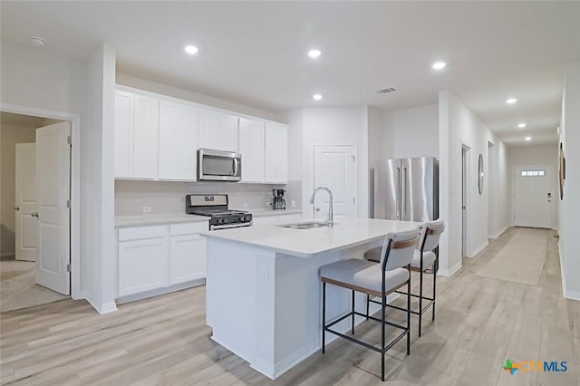 kitchen with stainless steel appliances, an island with sink, white cabinetry, and sink