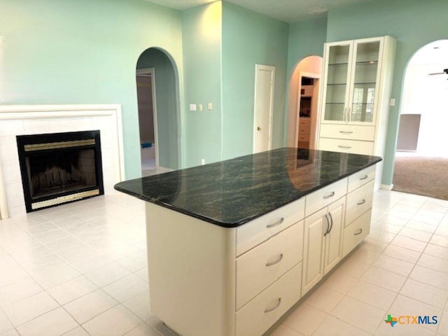 2772 Cloisters Dr, College Station, TX 77845 - kitchen with arched walkways, light tile patterned flooring, glass insert cabinets, a fireplace, and a center island