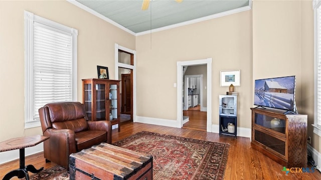 living area with a ceiling fan, crown molding, wood finished floors, and baseboards