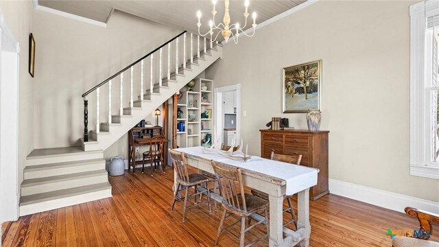 dining room with stairway, wood finished floors, baseboards, ornamental molding, and a notable chandelier