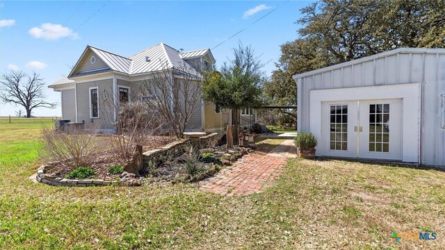 view of property exterior with an outbuilding, a standing seam roof, a yard, board and batten siding, and metal roof