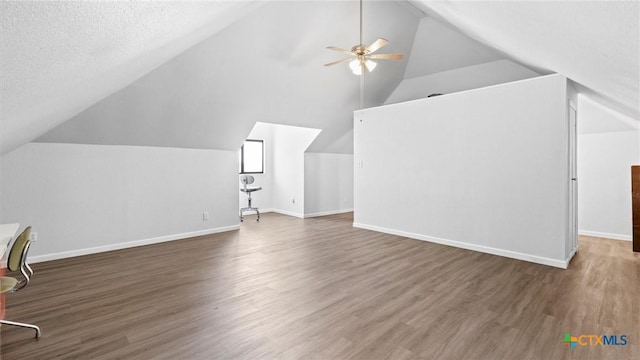 additional living space with lofted ceiling, a ceiling fan, a textured ceiling, wood finished floors, and baseboards