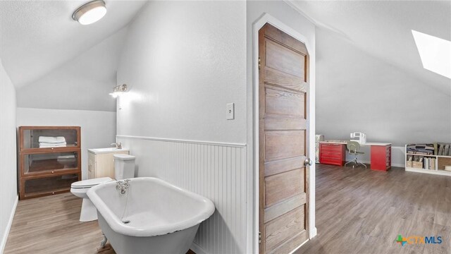 bathroom with wood finished floors, a wainscoted wall, vaulted ceiling with skylight, a freestanding tub, and toilet