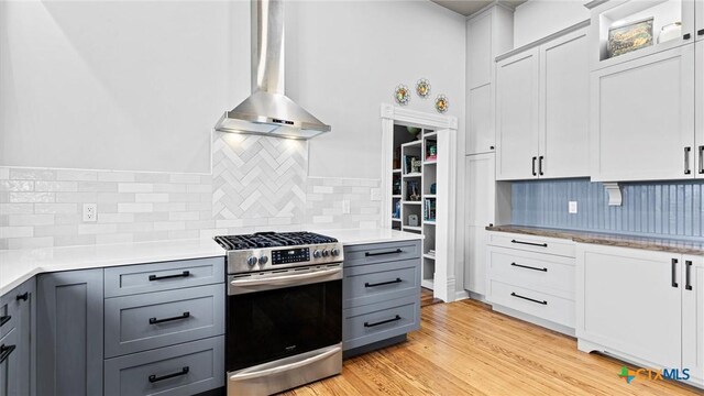 kitchen featuring gas range, wall chimney exhaust hood, light wood-type flooring, and gray cabinetry