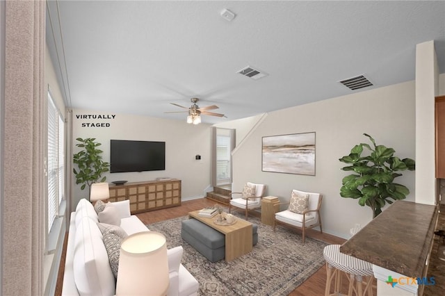 living area featuring ceiling fan, visible vents, baseboards, and wood finished floors