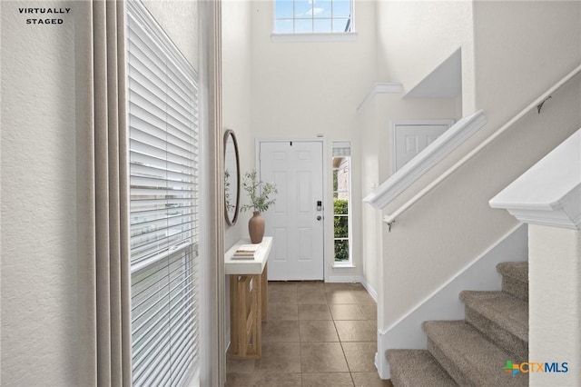 tiled foyer featuring stairs, plenty of natural light, and a towering ceiling